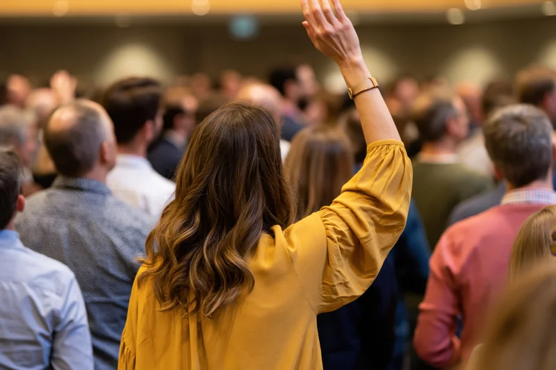 Woman raising hand in a crowded event audience viewed from behind