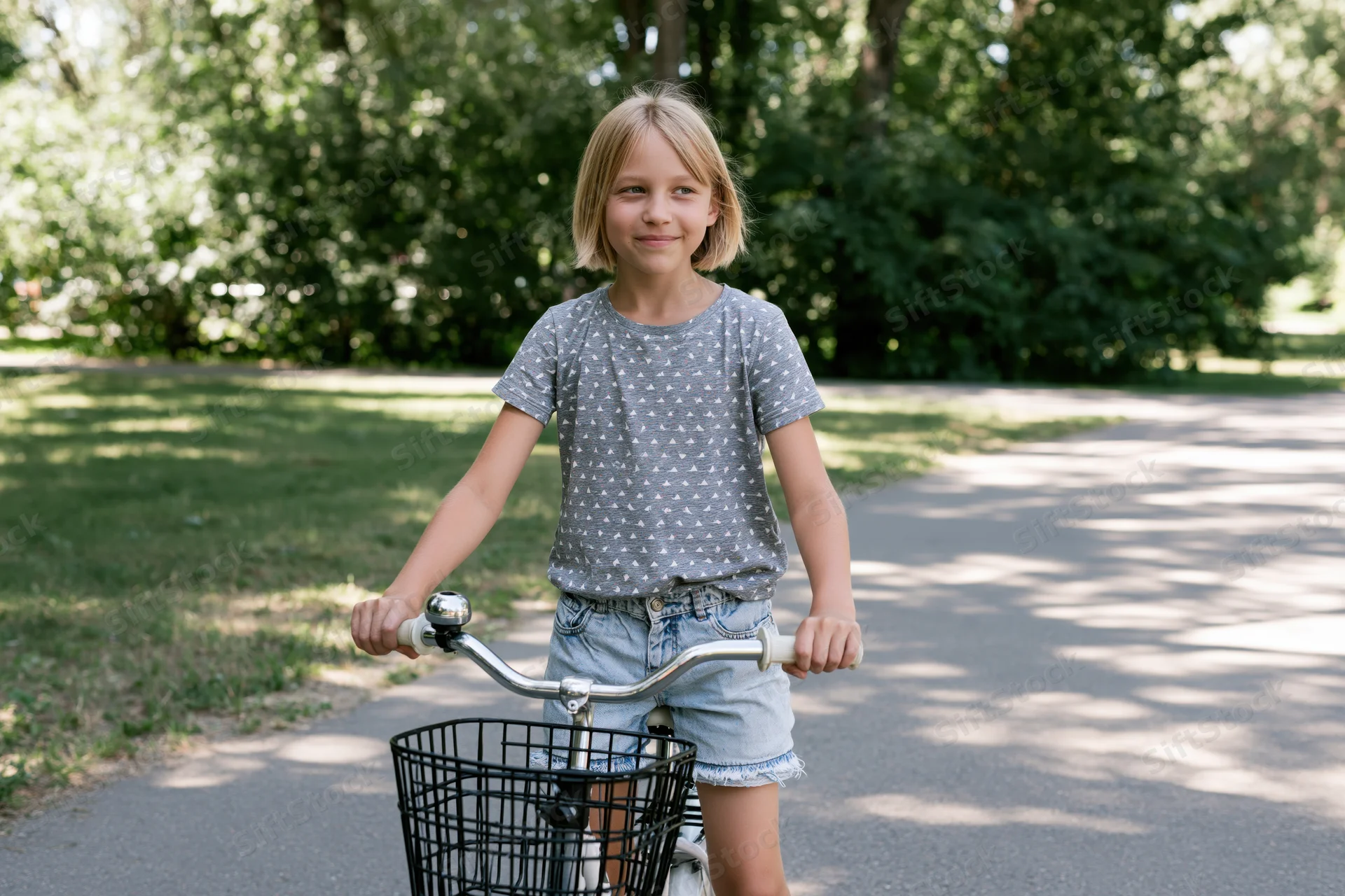 Young girl smiling while riding a bicycle on a paved path in a park