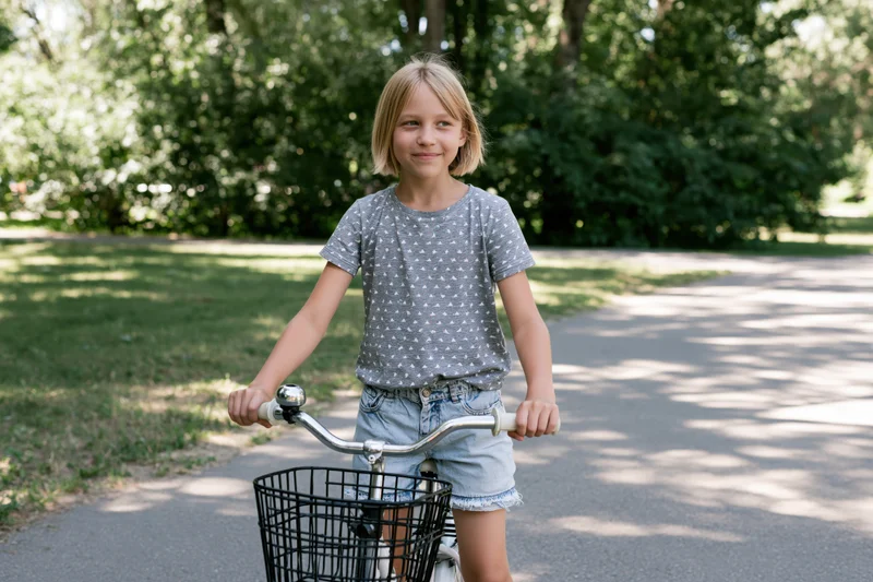 Young girl smiling while riding a bicycle on a paved path in a park
