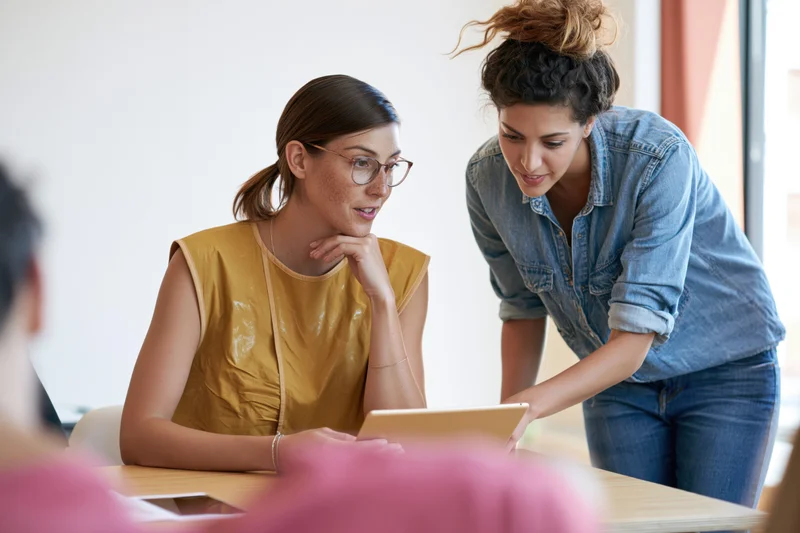 Two women collaborating on a tablet in a bright casual office workspace