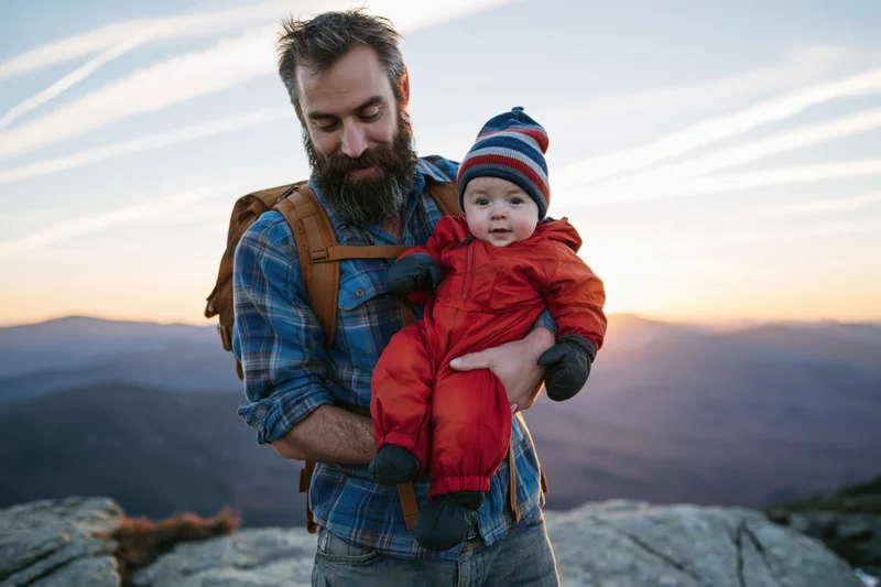 Bearded man holding baby on mountain summit at sunset