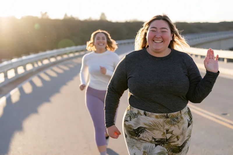 Two women running on a bridge at golden hour, one waving and smiling