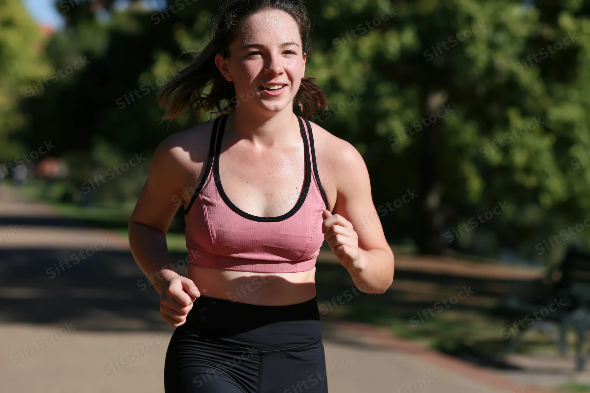 Young woman running on a park path in sportswear, smiling with motion blur in sunlight