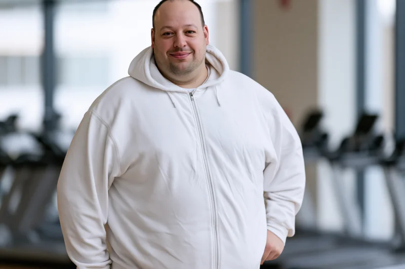 Overweight man smiling in white zip-up hoodie at gym
