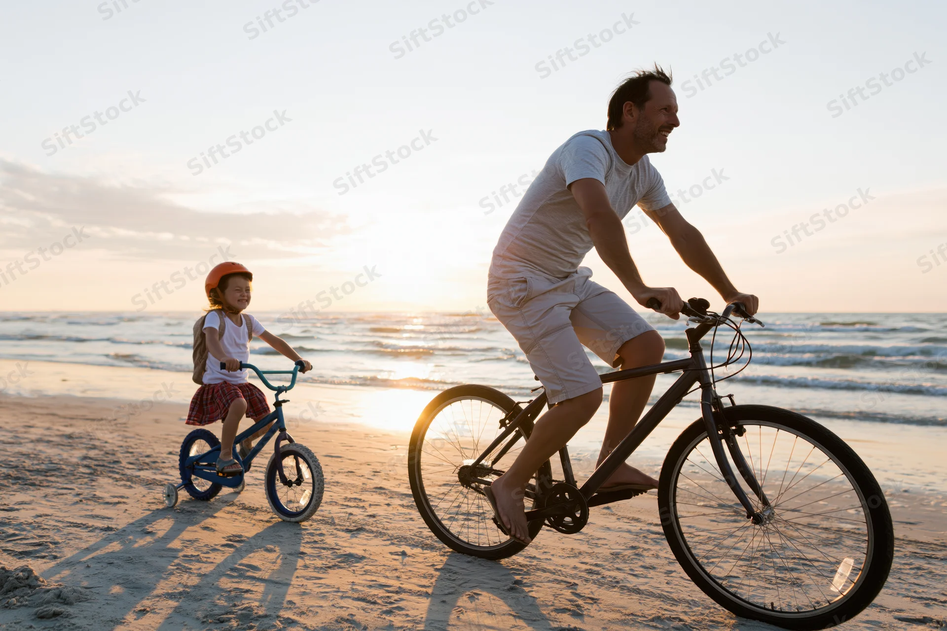 Father and daughter cycling on a sandy beach at sunset