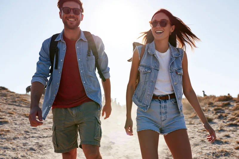 Couple hiking on a desert trail smiling in sunglasses with backpacks