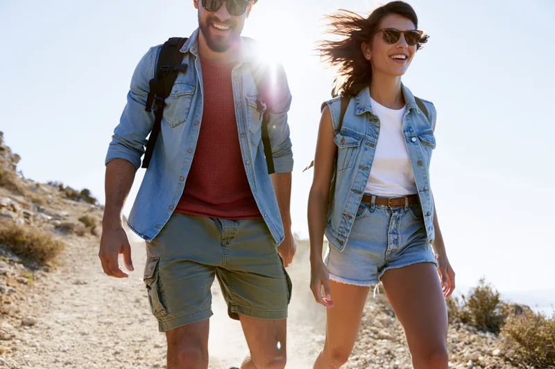 Couple hiking on a rocky trail in bright sunlight wearing denim and sunglasses