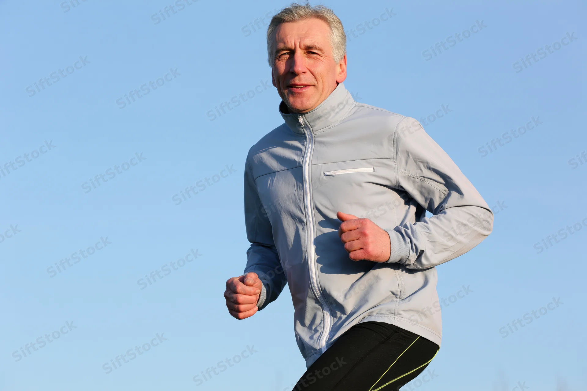 Middle-aged man running outdoors in sportswear against a clear blue sky