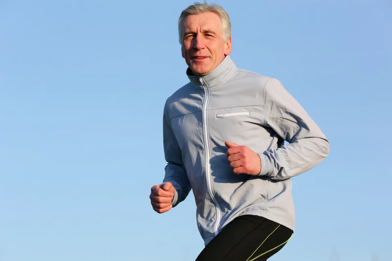 Middle-aged man running outdoors in sportswear against a clear blue sky