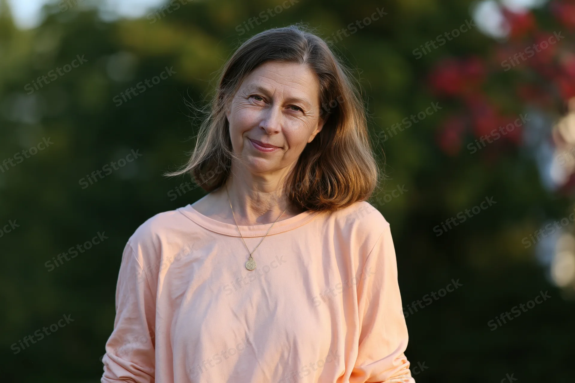 Middle-aged woman smiling softly outdoors in a garden setting