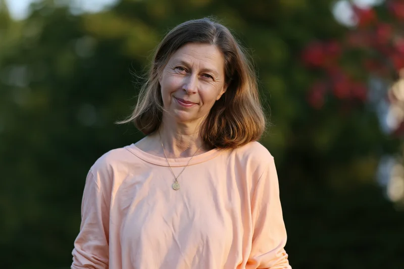 Middle-aged woman smiling softly outdoors in a garden setting