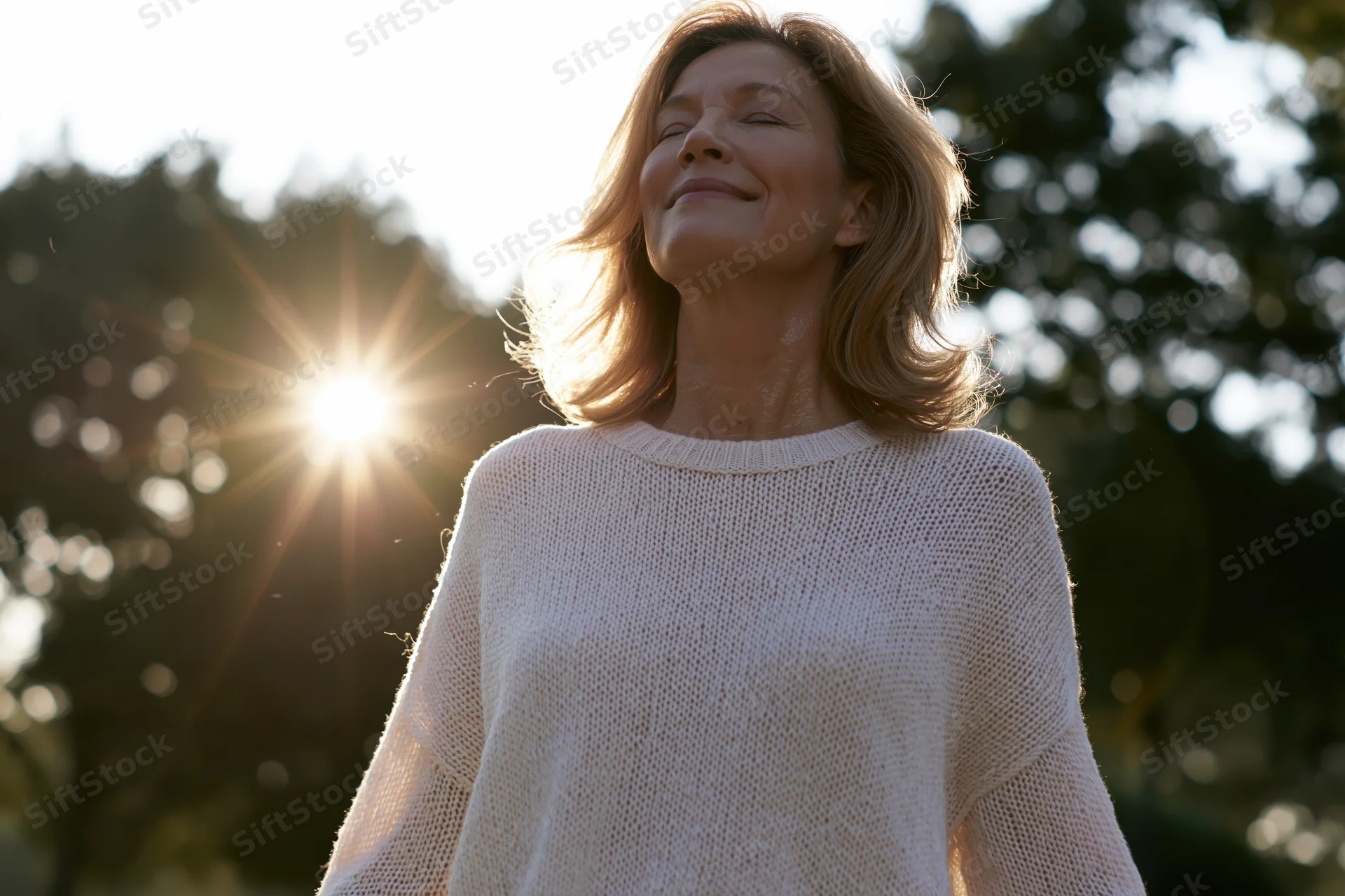 Middle-aged woman smiling with eyes closed in sunlight outdoors