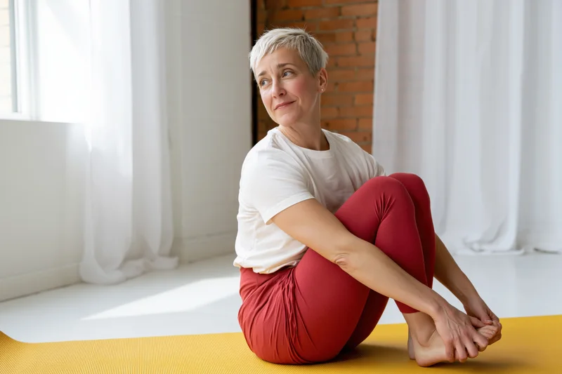 Woman stretching seated on yoga mat in home setting