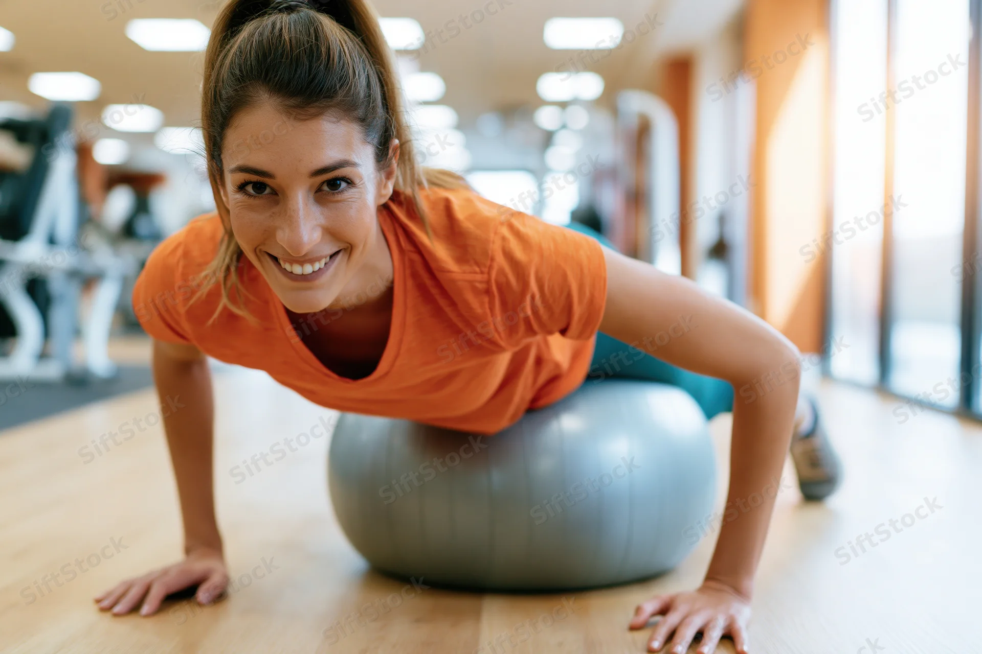 Woman doing pushup on stability ball in gym smiling at camera