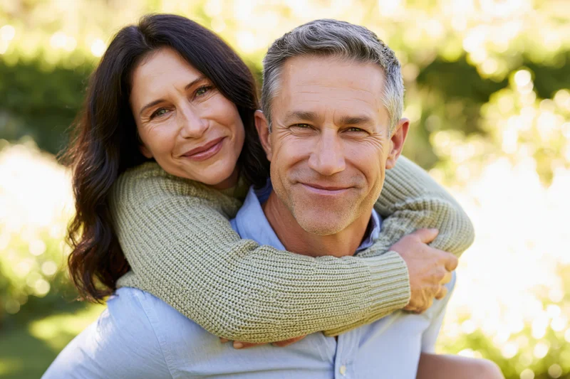 Woman embracing man from behind in a sunny park setting
