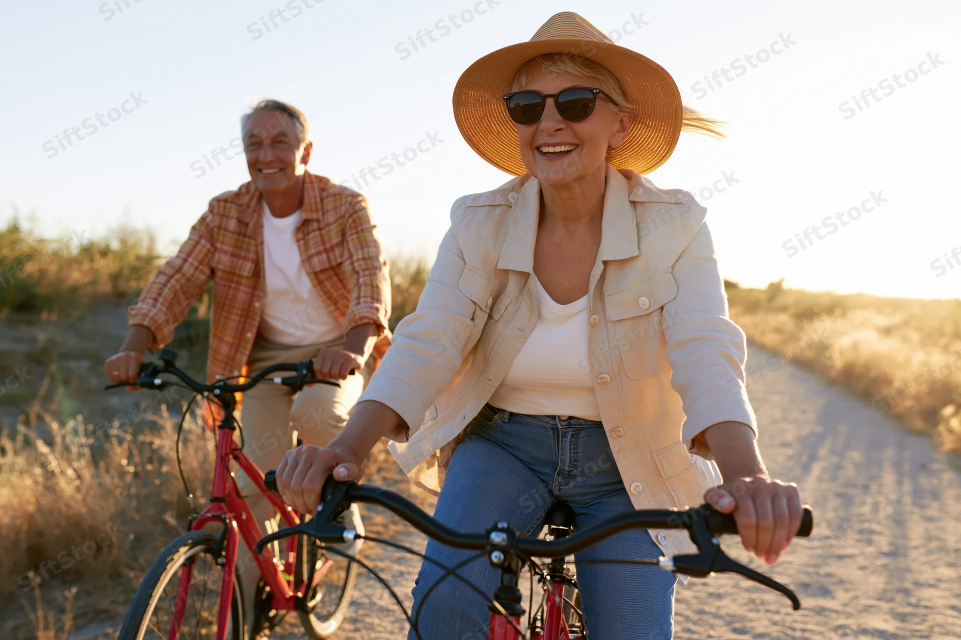 Smiling senior couple cycling on a sandy path at sunset