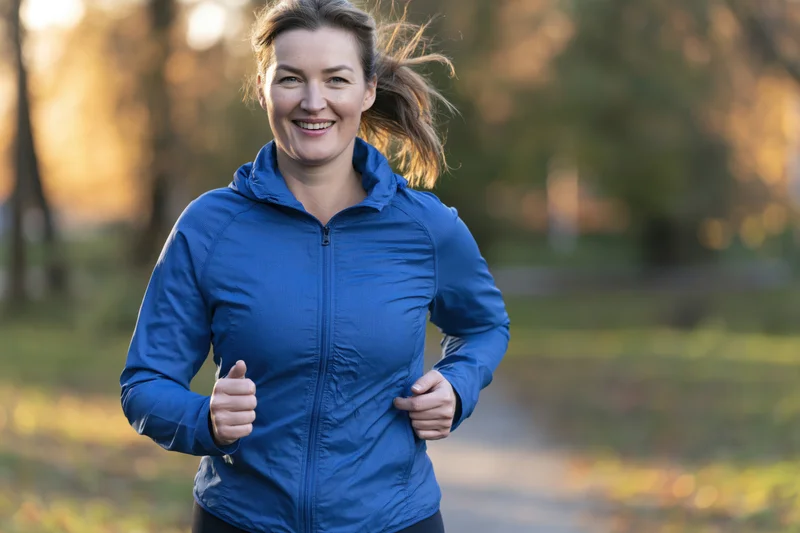 Woman running on a park trail smiling in sportswear during golden hour