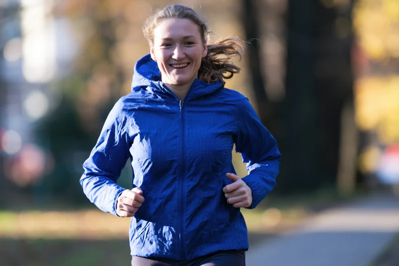 Woman running outdoors on a paved path in a park during autumn