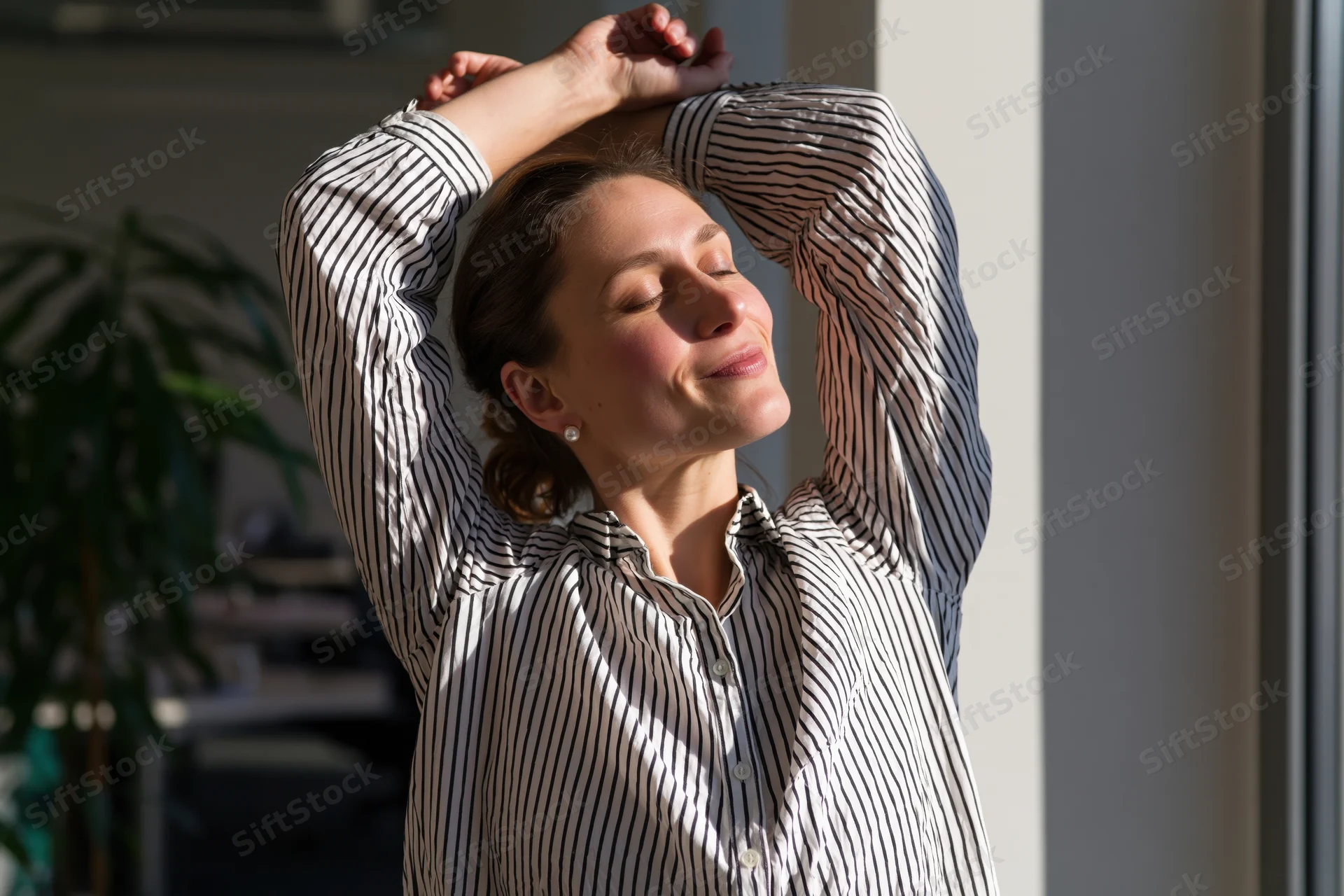 Woman stretching with arms raised near window in office space