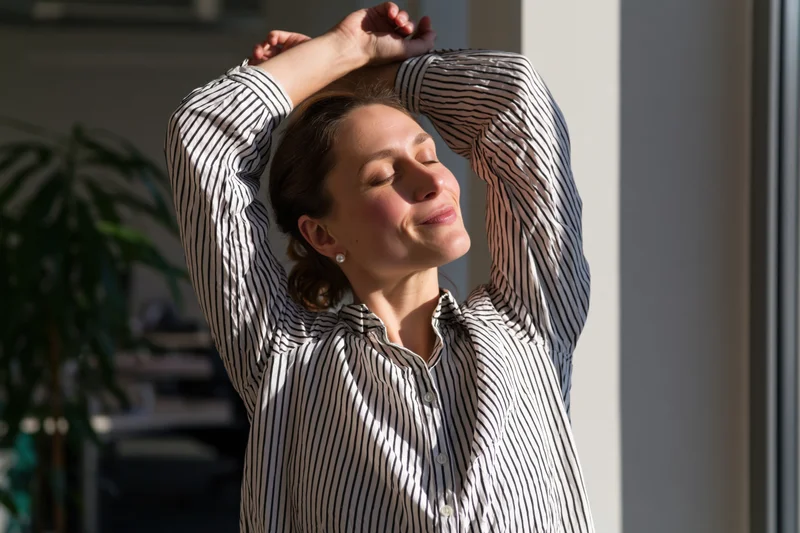 Woman stretching with arms raised near window in office space