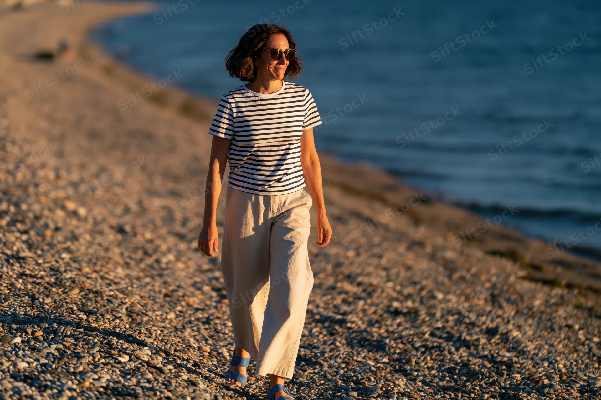 Woman walking along pebble beach at sunset