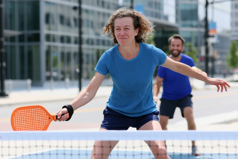 Woman playing pickleball on an outdoor court in an urban setting