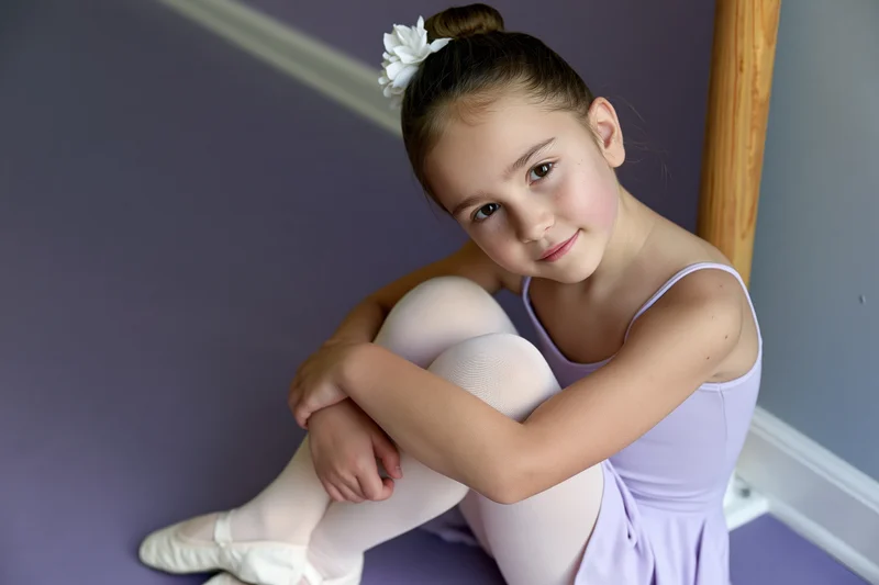 Young girl in ballet attire sitting on floor hugging knees in studio