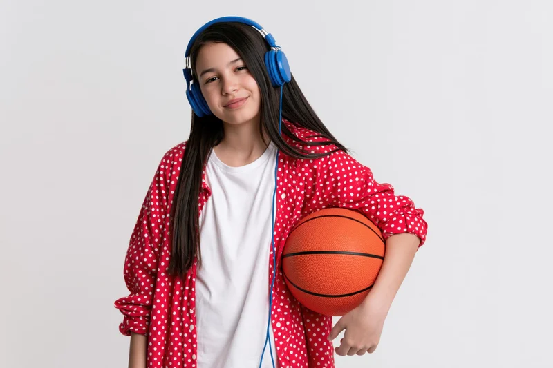 Smiling girl holding basketball and wearing blue headphones in studio setting