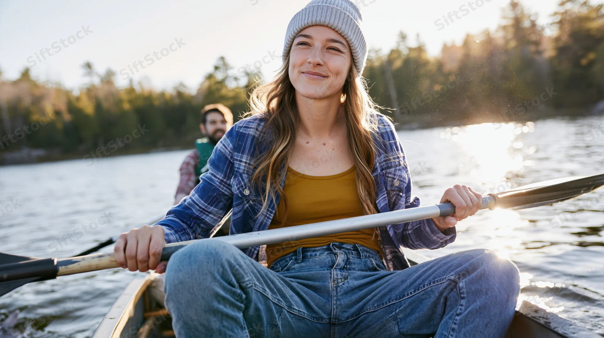 Young woman paddling a canoe on a lake at golden hour, smiling, surrounded by forest