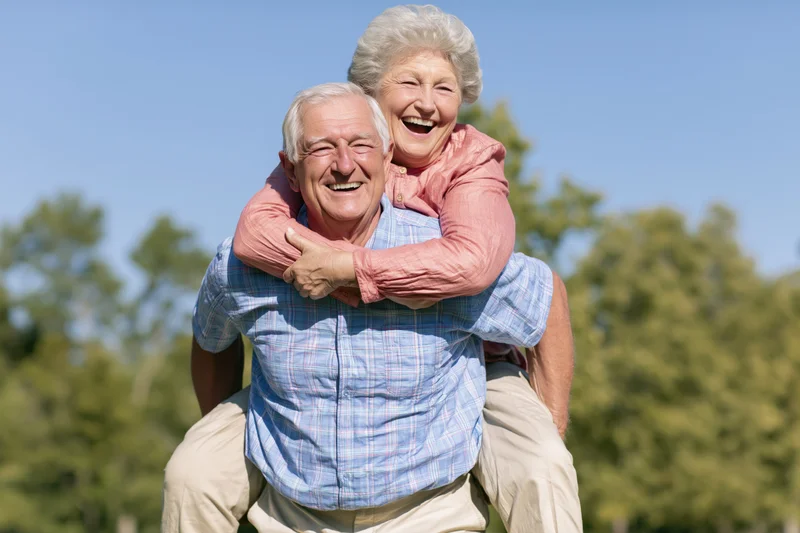 Senior couple laughing while giving piggyback ride outdoors in park