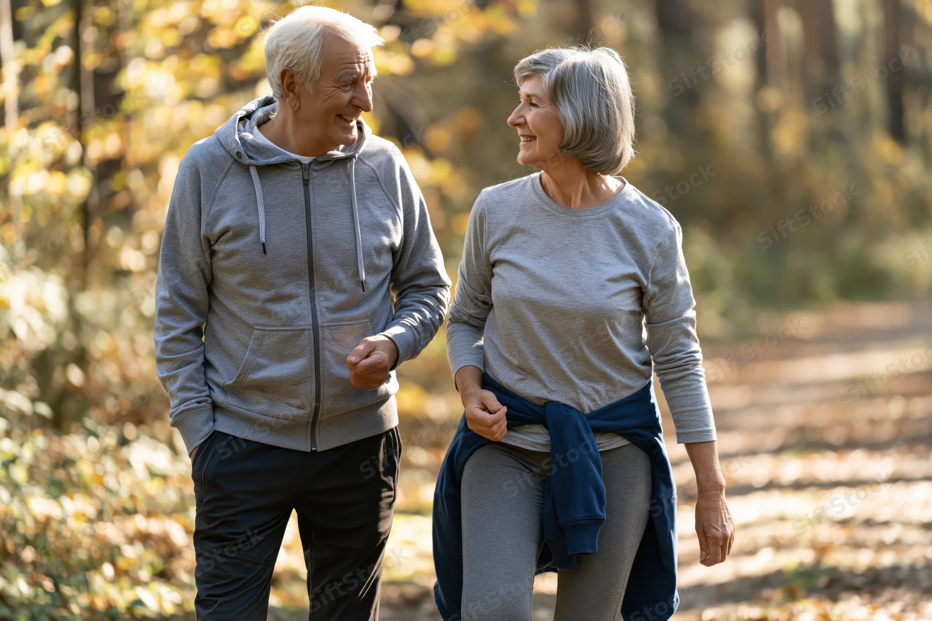 Elderly couple walking and smiling together on a forest trail in autumn