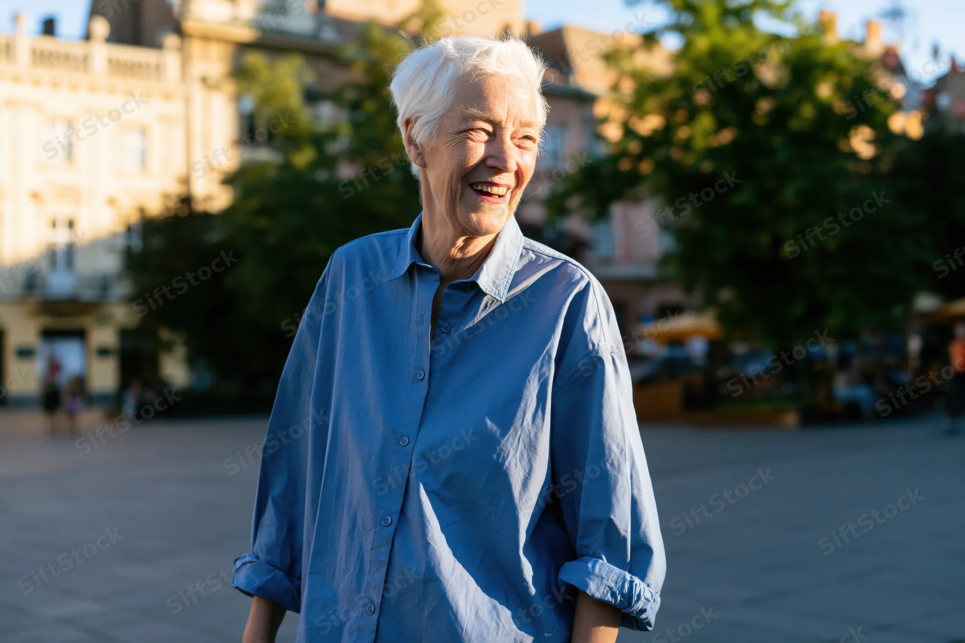 Elderly woman smiling outdoors in a city square wearing a blue shirt