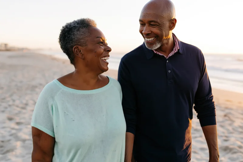 Senior africanamerican couple smiling at each other on sandy beach at sunset