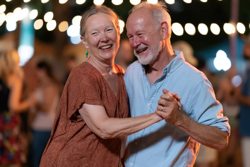 Older couple dancing together outdoors at night under string lights, smiling and laughing