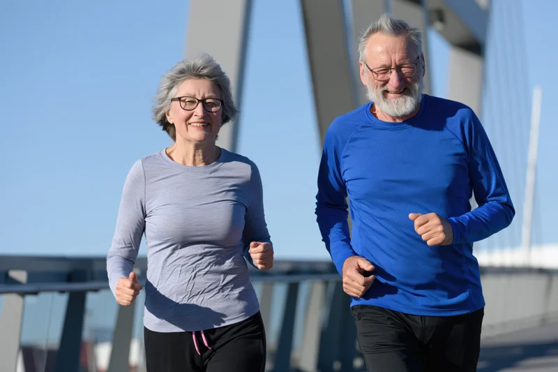 Older couple jogging side by side on a bridge in daylight