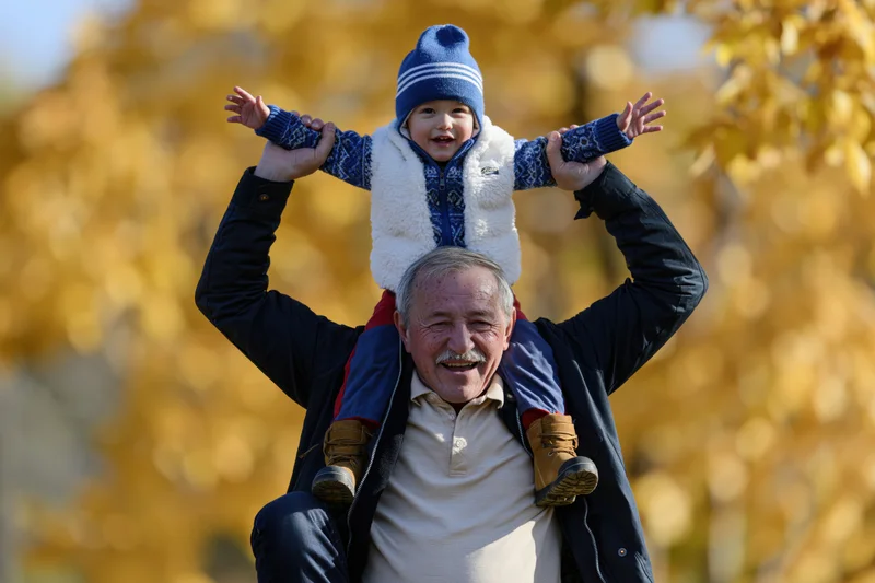 Grandfather carrying toddler on shoulders in autumn park