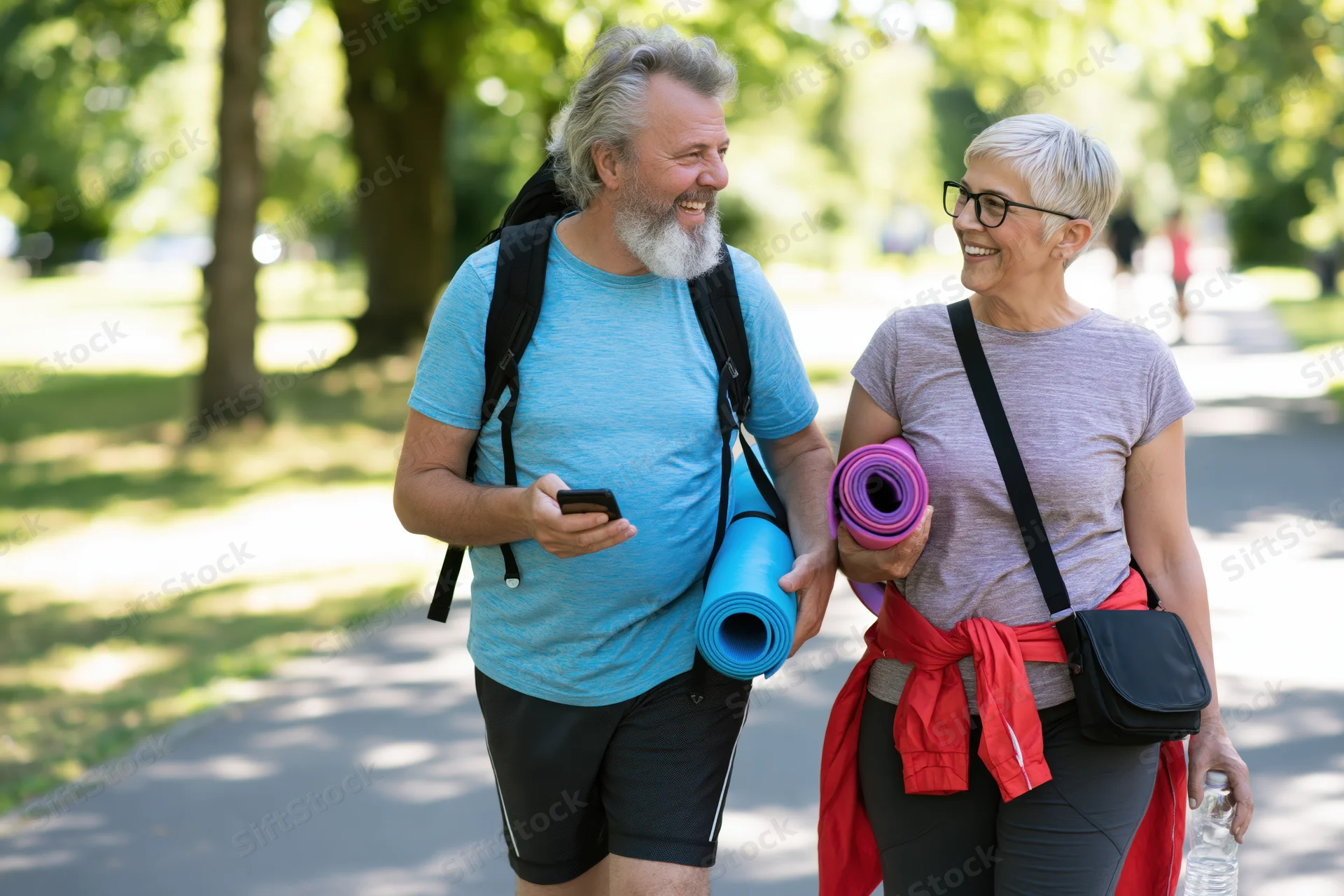 Senior couple walking and smiling in a park while carrying yoga mats and water bottles
