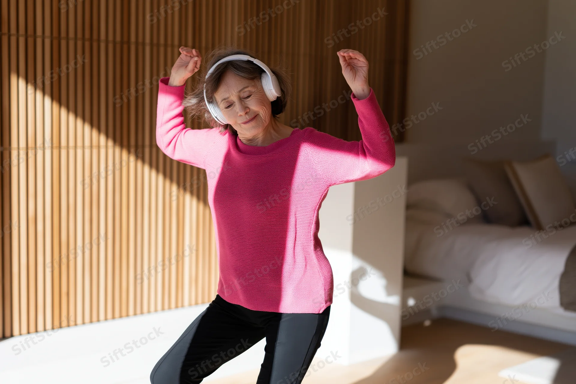 Senior woman dancing with headphones in a sunlit bedroom