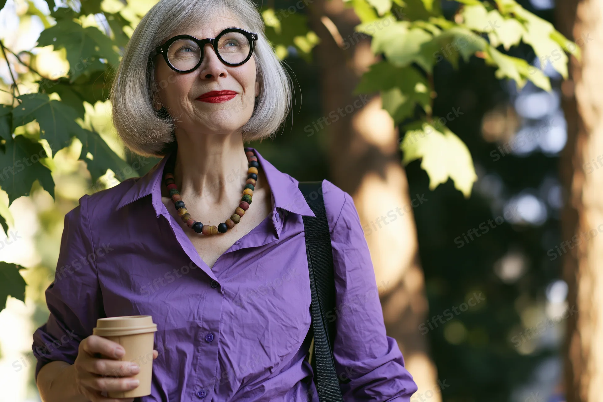 Senior woman holding coffee cup outdoors in park, smiling and looking up through tree leaves
