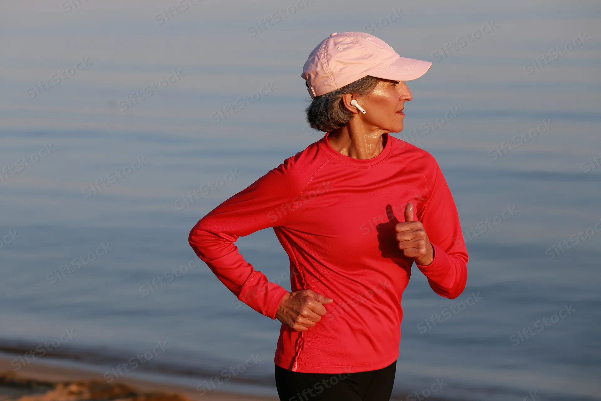 Senior woman running along the beach with earbuds in profile view