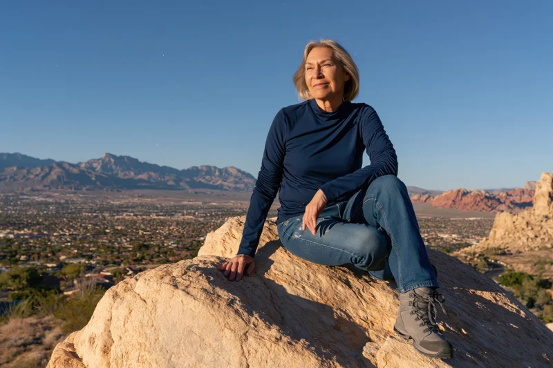 Senior woman sitting on a rock overlooking a desert valley with mountains and city in the distance