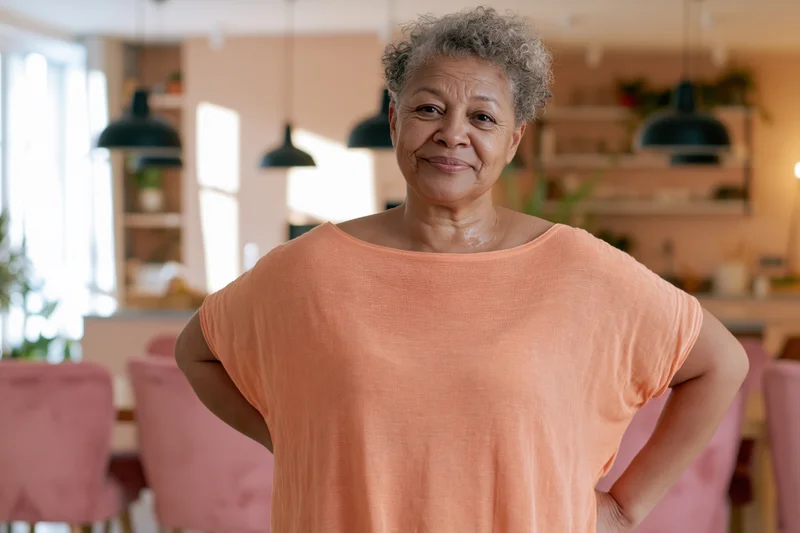 Senior woman smiling with hands on hips in a warm kitchen interior