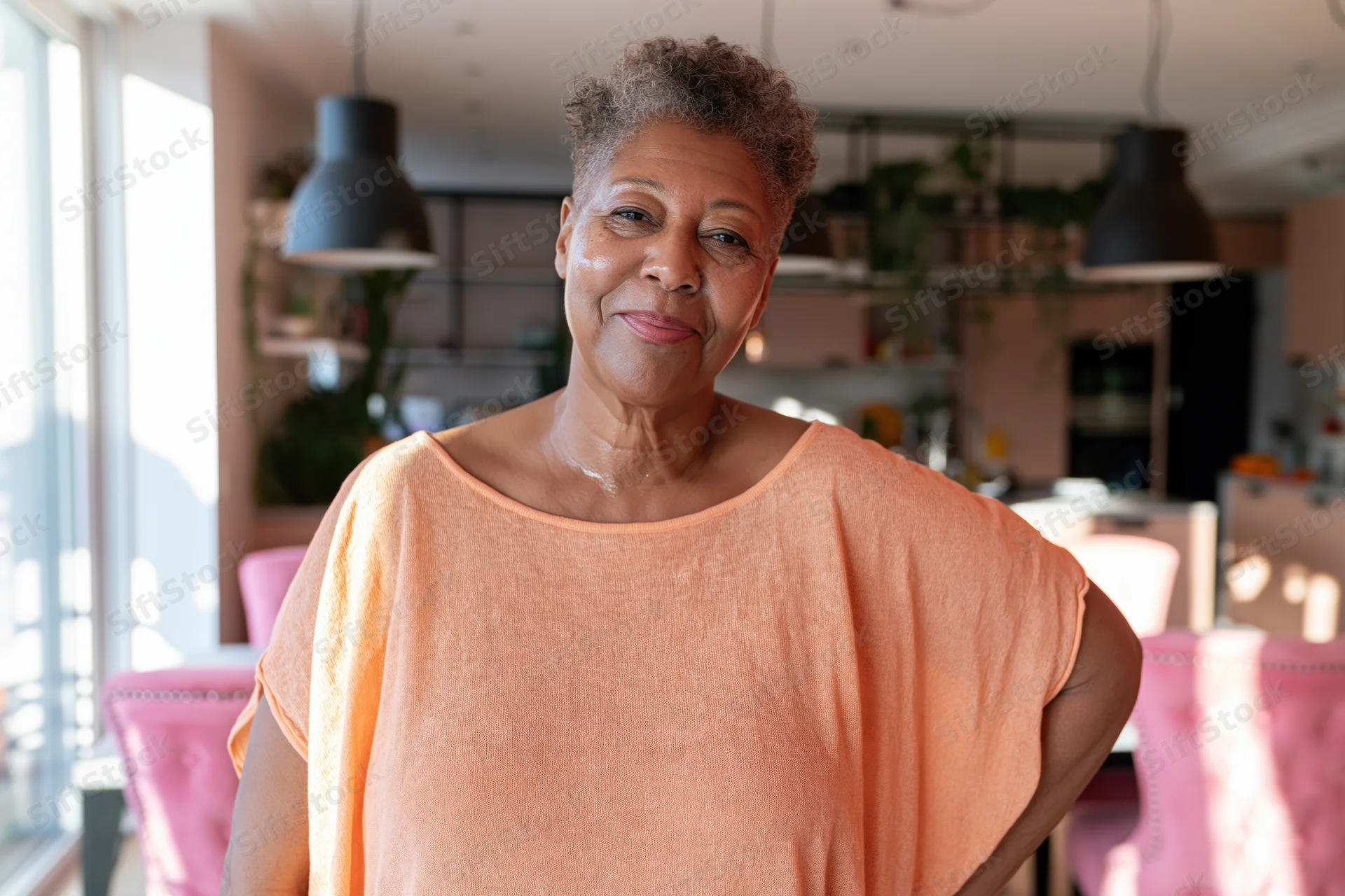 Senior africanamerican woman smiling in kitchen with pink chairs and pendant lights