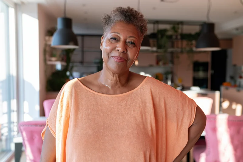 Senior africanamerican woman smiling in kitchen with pink chairs and pendant lights