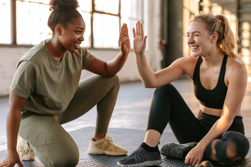 Two women high-fiving on a gym mat during a workout session