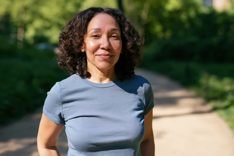 Middle-aged woman smiling outdoors on a park path surrounded by greenery