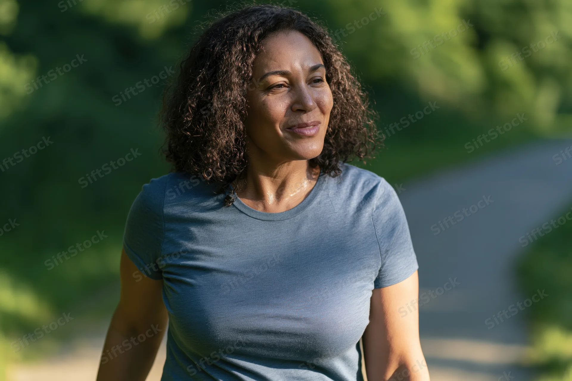 Middle-aged woman walking along a park path smiling in natural sunlight