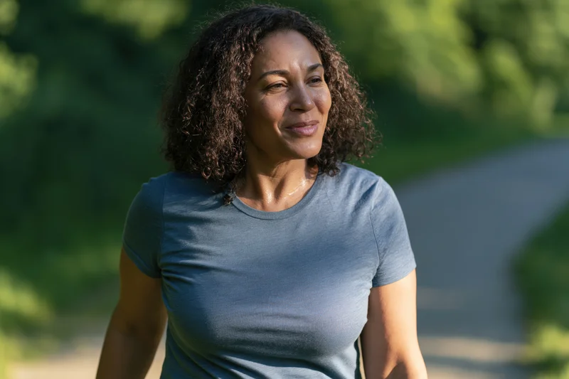 Middle-aged woman walking along a park path smiling in natural sunlight