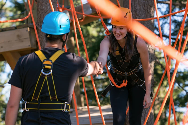 Woman and man shaking hands on a high ropes course in a forested outdoor setting