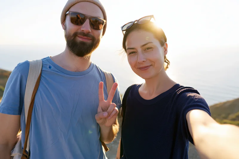 Couple taking a selfie outdoors with ocean and mountains in the background